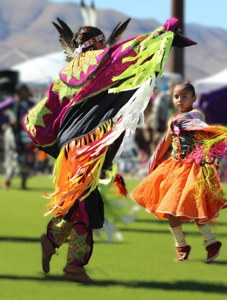 Snow Mountain Paiute Pow Wow Grand Entry as young girl is enthralled by the technique of another dancer as they dance together as seen in Powwows: Cedar; Cedar City; Duck Valley; Elko; Ely; Fallon; Fort Mojave; Goshute; Moapa; Muckleshoot; Nevada Day; Numaga; Red Dress; Sacred Visions; Stewart; Sycuan; UNLV;  UNR; Univ. of Nev. Reno; and Walker River; Western Navajo Fair.