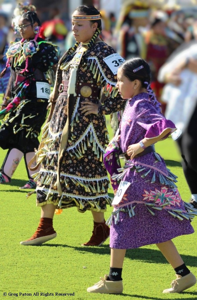 Snow Mountain Paiute Pow Wow Grand Entry as three young Jingle Dress performers lock step as seen in powwows: Cedar Band; Cedar City; Duck Valley; Elko; Ely; Fallon; Fort Mohave; Fort Mojave; Goshute; Las Vegas; Snow Mountain; Las Vegas Snow Mountain; and Las Vegas Paiute.