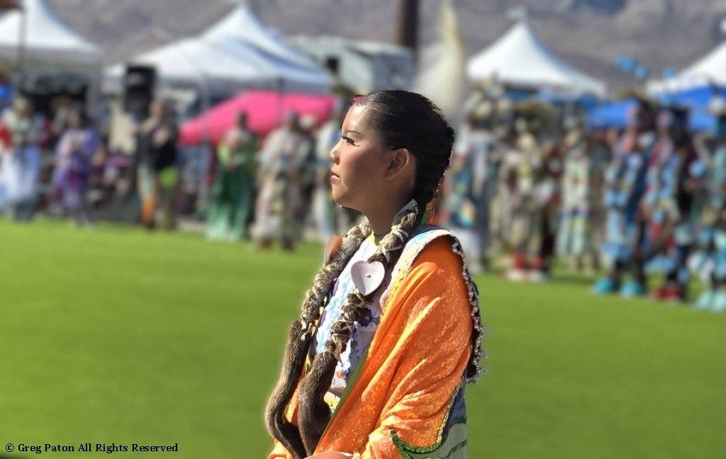 A Native American woman listens to the prayers in Grand Entry as seen in powwows: Apache; Apache Nation; Arapaho; Blackfeet; Blackfeet Nation; Blackfoot; Black Hills; Cherokee; Cherokee Nation; and Cheyenne.